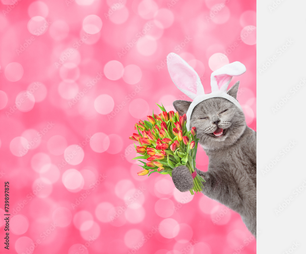 Poster happy kitten wearing easter rabbits ears holds holds bouquet of tulips and looks from behind empty w