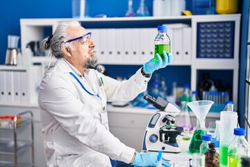 Middle age grey-haired man scientist looking bottle at laboratory