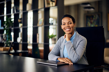 A smiling African businesswoman, posing for the camera, sitting at the office.
