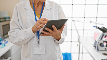 A mature woman healthcare professional examines a tablet in a modern laboratory setting.