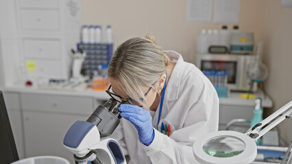 A caucasian woman scientist examining samples through a microscope in a laboratory setting.