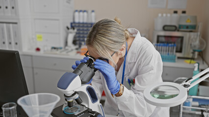 A focused young woman scientist examining a sample under a microscope in a modern laboratory...