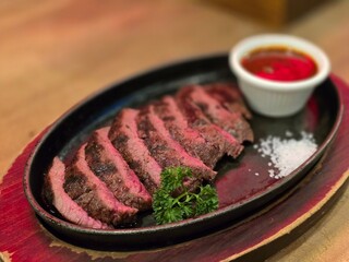 Grilled Juicy steak medium rare beef with herbs and spices on pan hot served with salt and brown sauce on wooden table.