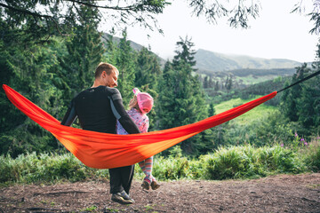 happy father with daughter on hammock mountains on background