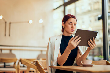 A focused woman working as a manager of the restaurant, using a digital tablet, and drinking coffee.