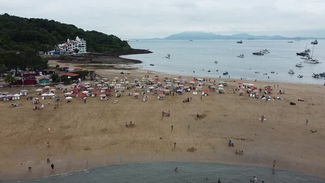 Aerial drone: Flying over the beach of Taboga Island, with a view of umbrellas of people enjoying the sunny day. Additionally, you can see boats in the bay and ships waiting to enter the Panama Canal.