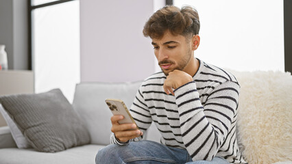 Serious young arab man doubting his next idea, deeply immersed while texting on his smartphone,...
