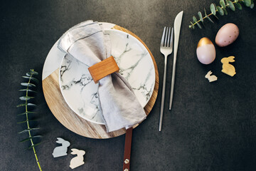 Easter table setting concept. Plate, easter eggs, cutlery and branches of eucalyptus on dark background table. Flat lay, top view - 739904080