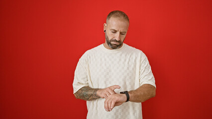 Late again! serious-faced young man checking watch isolated over red background, his expression...