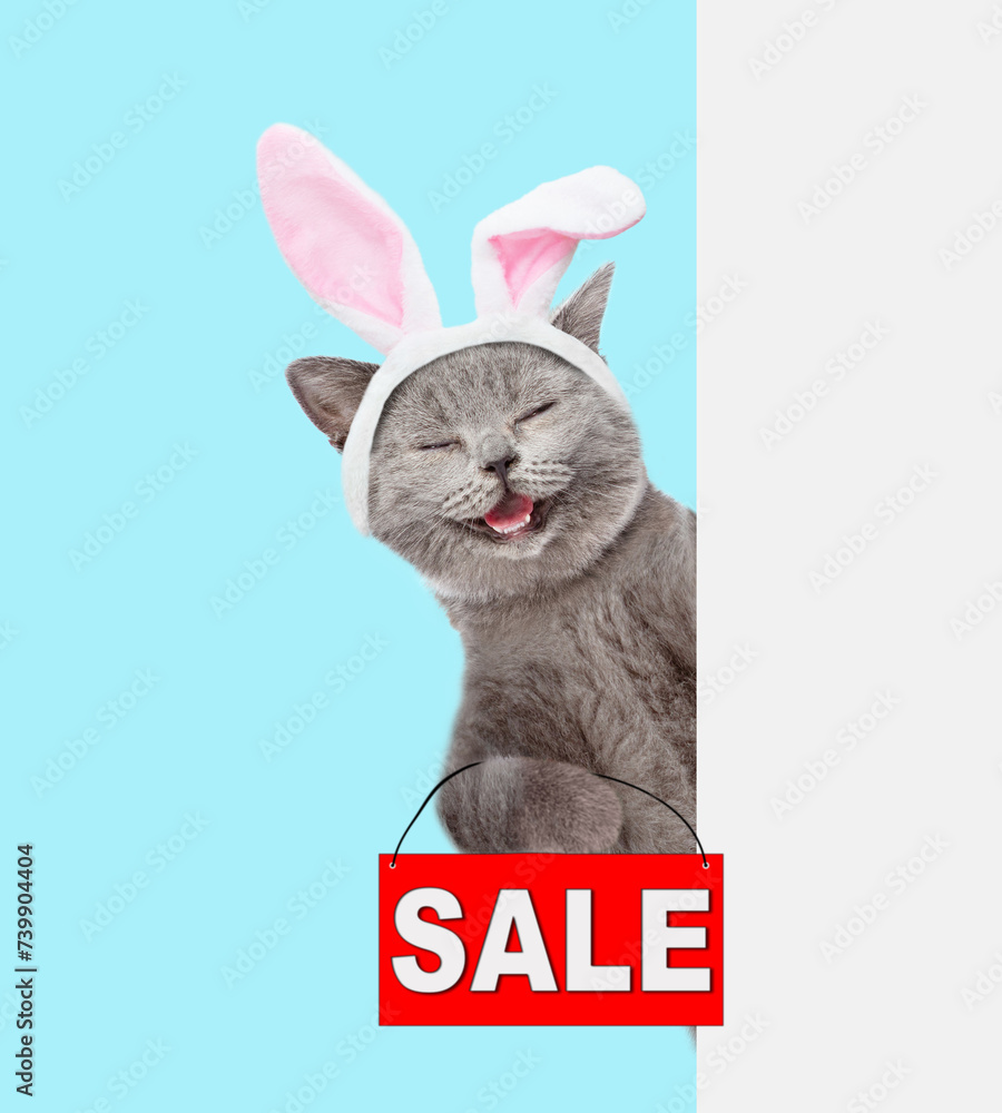 Aufkleber happy cat wearing easter rabbits ears holds sales symbol behind empty white banner. isolated on blue