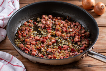 Golden fried onions with pieces of bacon in a pan on a wooden table