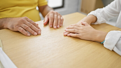 United in unity, hispanic man and woman holding hands, sitting together at home table in living room interior for a meaningful indoor meeting