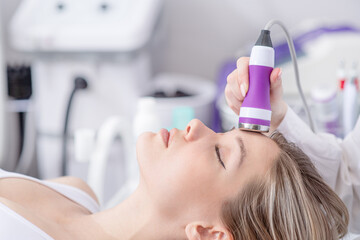 Woman receiving electroporation phonophoresis facial therapy at beauty spa salon. Hardware face...