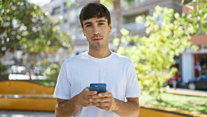 Cool looking young hispanic man, with serious expression, deeply engrossed in texting on smartphone...