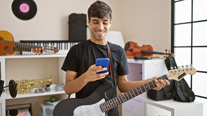 Attractive young hispanic man, an electric guitar musician, charmingly smiling while texting on his...