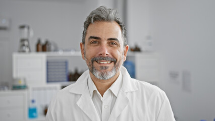 Confident young hispanic man, a smiling scientist with grey hair, standing in the lab, handsomely...
