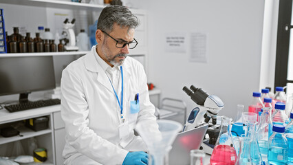 Serious grey-haired young hispanic man a scientist, engrossed in his work while sitting at...
