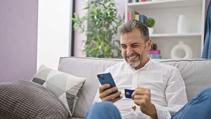 Smiling young grey-haired hispanic man casually shopping online, safely paying with credit card on...