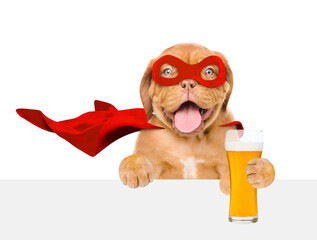 Happy Mastiff puppy wearing superhero costume holds mug of light beer above empty white banner....