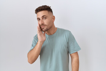 Hispanic man with beard standing over white background hand on mouth telling secret rumor, whispering malicious talk conversation