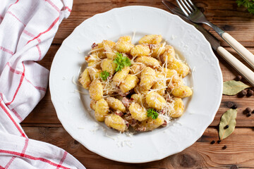 Close up view of potato gnocchi with bacon and sauce in a white plate on a wooden table. Top view, flat lay