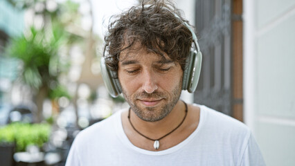 A handsome young man listening to music with headphones on an urban city street, exuding a relaxed vibe.