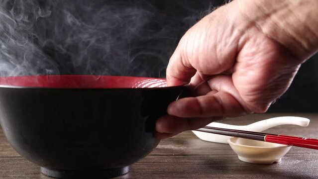 Smoke vapour fog rising flowing out of miso soup black red white bowl on dark black background