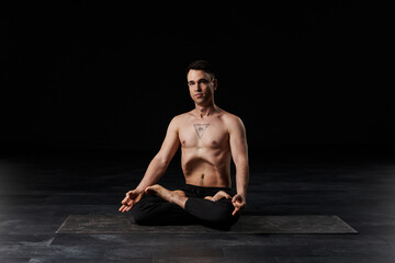 The man in lotus meditation, abdomen vacuumed, bears an all-seeing eye tattoo on his chest,...