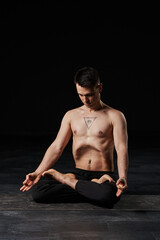In a lotus stance, practicing stomach vacuum, the man's chest inked with an all-seeing eye,...