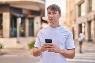 Young caucasian man smiling confident using smartphone at street