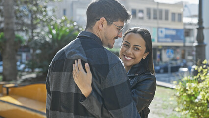 A smiling couple in love embraces on a sunny city street, conveying a sense of joy and urban...
