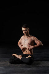 The man in lotus pose, focusing on stomach vacuum, displays an all-seeing eye tattoo on his chest,...