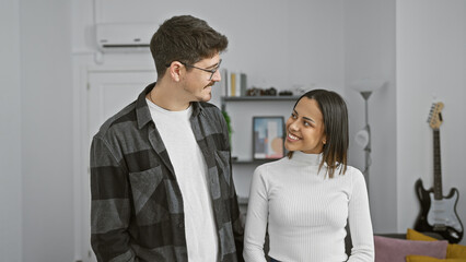 A smiling couple engaging in a warm look inside a modern living room decorated with a guitar
