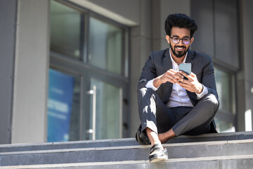 Dark-haired hindu man sitting on the steps with a phone in hands