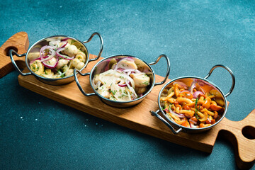 Pickled mushrooms with onions and vinegar in a metal bowl. Cold snacks. Restaurant serving. Close up. On a dark stone background.