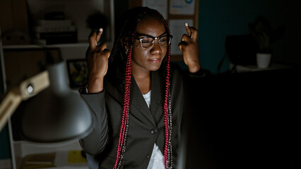 Serious, relaxed african american woman crossing her fingers for luck in the office, a beautiful...