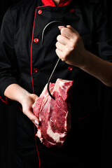 Raw steak on a meat hook in the hands of a chef. Meat. On a black background.