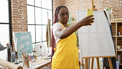 Beautiful african american woman artist making a selfie with smartphone in art studio while relaxed...