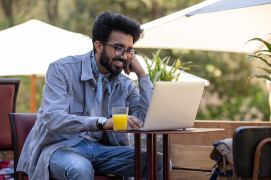 Dark-haired young hindu man working on laptop in a cafe