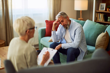 A stressed adult male patient rubbing his forehead while talking about his problems to his...