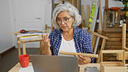 Mature woman carpenter with grey hair discussing project in workshop indoors.