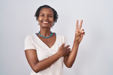 African woman with dreadlocks standing over white background smiling with happy face winking at the...