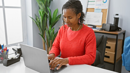African american woman working on a laptop in a modern office setting.