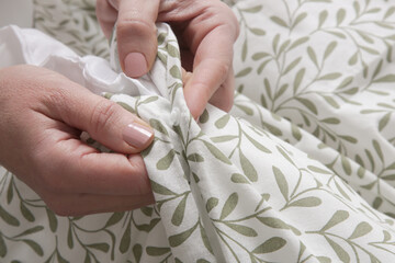 Woman is closing buttons on duvet cover while making the bed, close up	