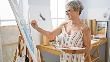 Mature woman artist painting on canvas in bright indoor studio