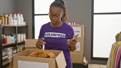 African american woman volunteer using a smartphone in a storeroom with boxes and supplies.