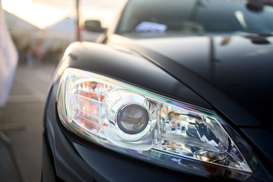 Berlin, Germany - August 20, 2022: Car Detail Shot of Mazda RX-8. Headlight front of black metallic car shot closeup on out of focus background with copyspace.