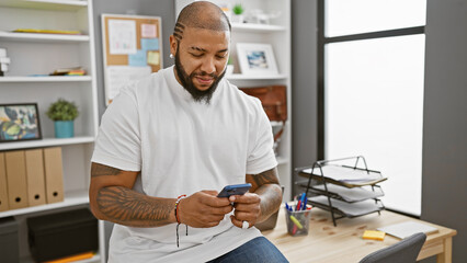 Smiling african american man with beard using smartphone in modern office setting.
