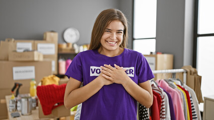 Confident young beautiful hispanic woman volunteer, chest ablaze with emotion, stands smiling in charity center, hands ready to work - obrazy, fototapety, plakaty