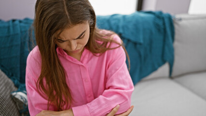 Beautiful young hispanic woman, resting on her cozy living room sofa, looking worried while...
